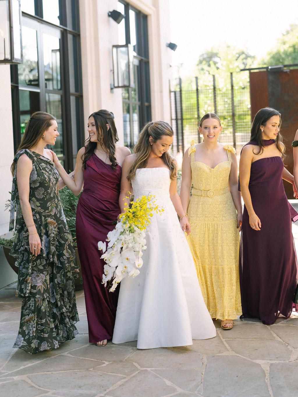 Bride with her attendants in jewel-toned gowns outside a stone building