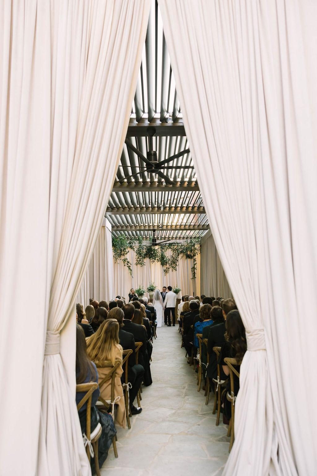 Ceremony aisle framed by tall white drapes with guests seated on either side