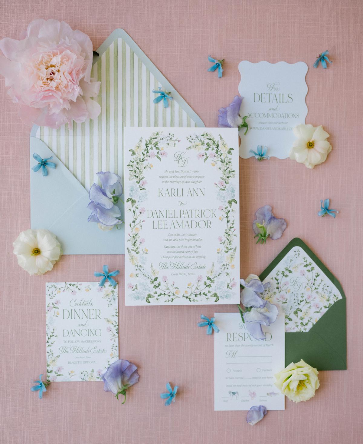 An invitation suite laid out with pressed flowers on a pink background