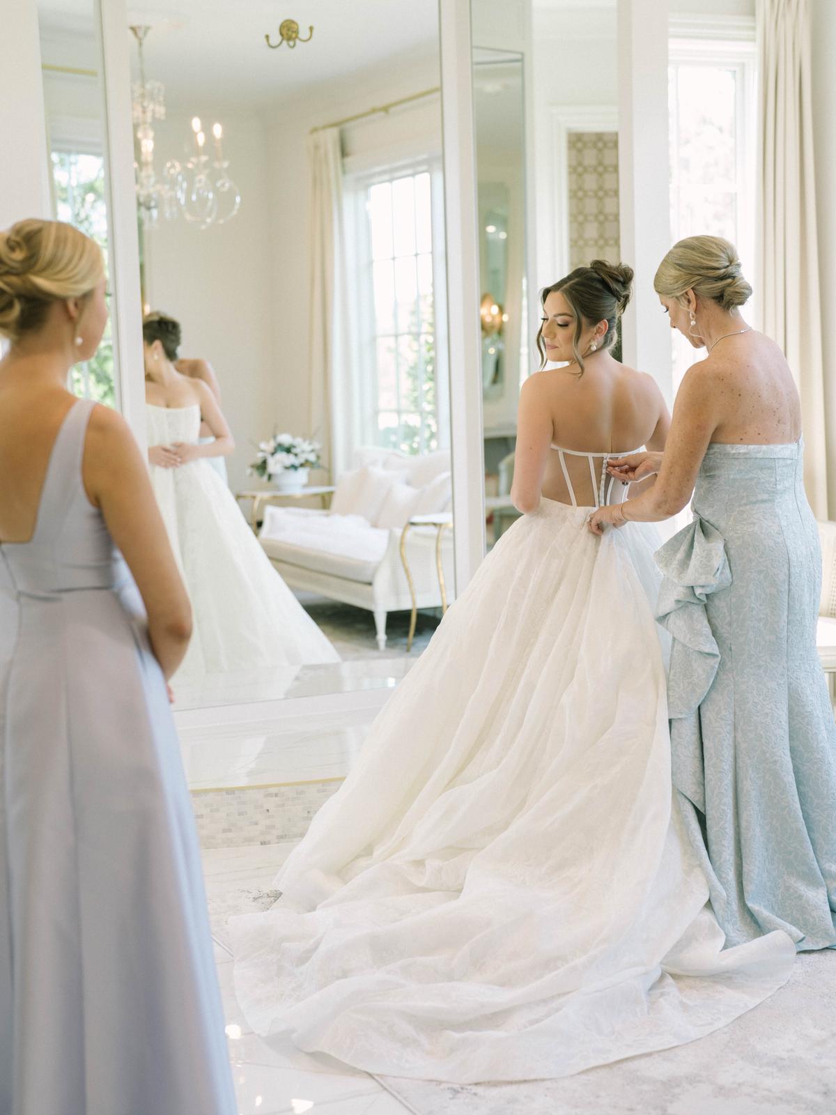 A bride in a veil being helped into her dress by an attendant