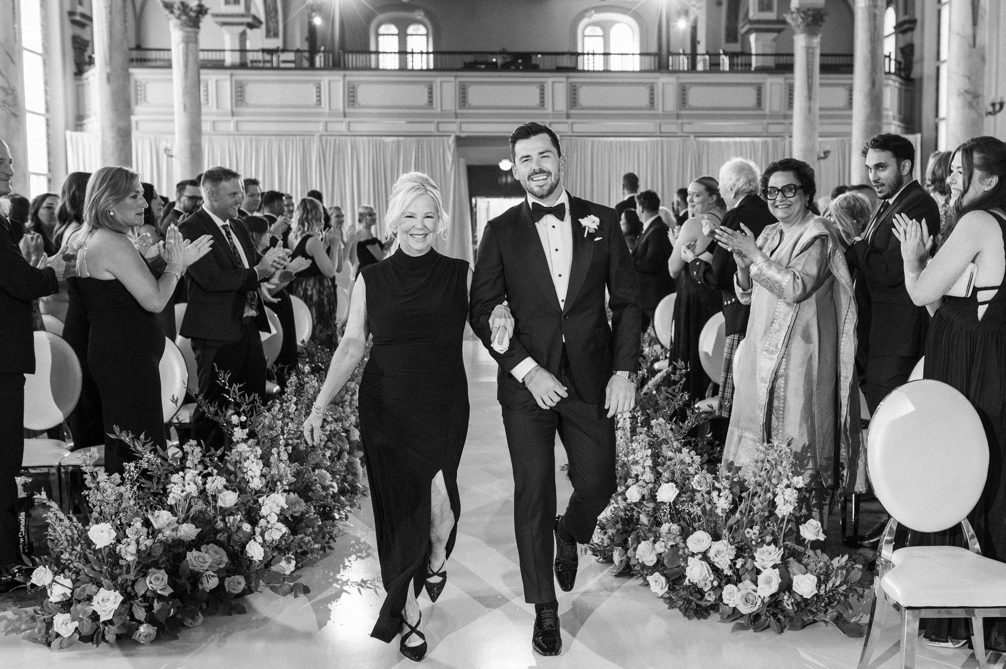 A couple recess down a flower-lined aisle through applauding guests in the ornate hall at Théâtre Cartier