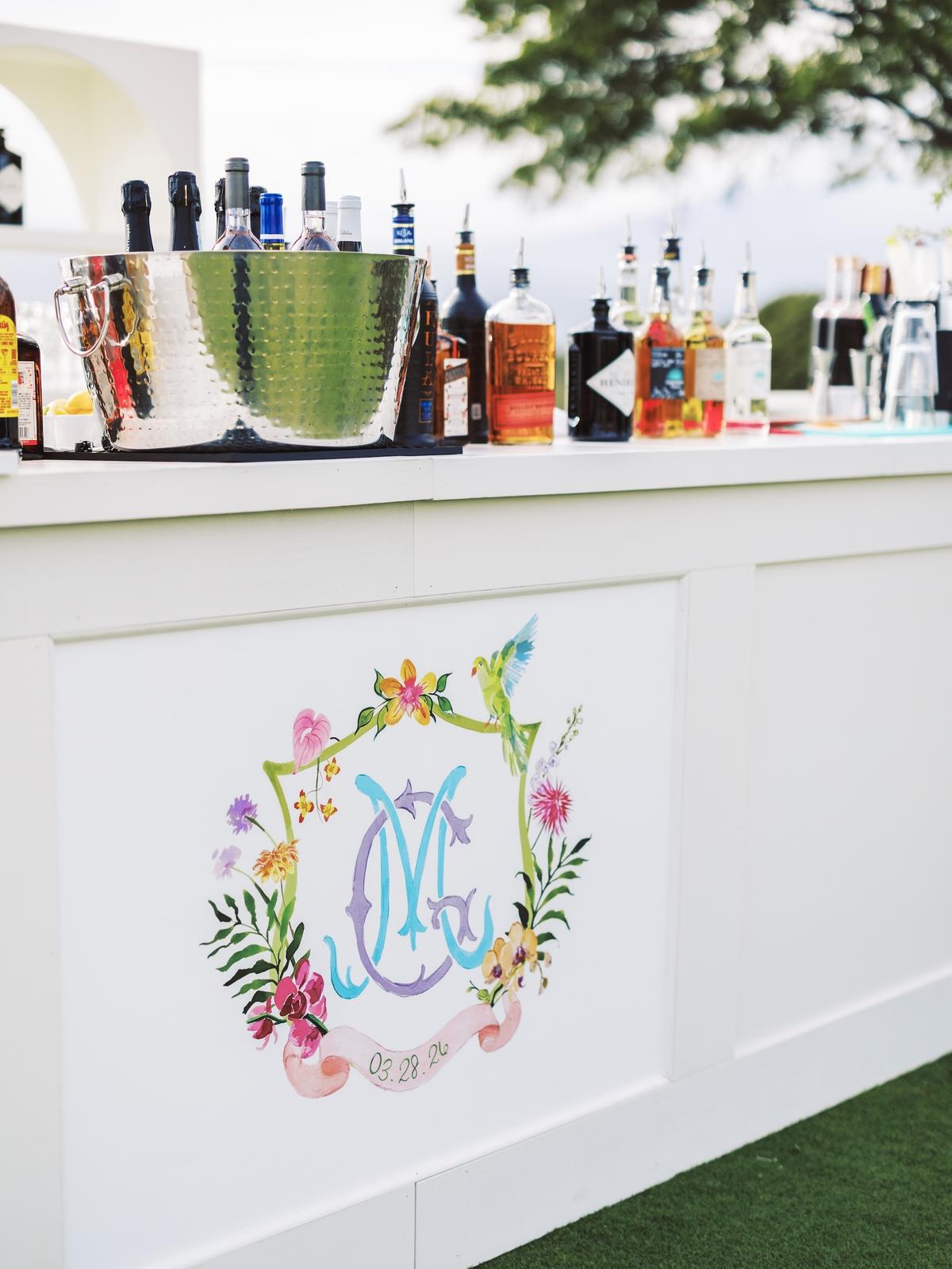 A white outdoor bar painted with a colorful floral monogram crest