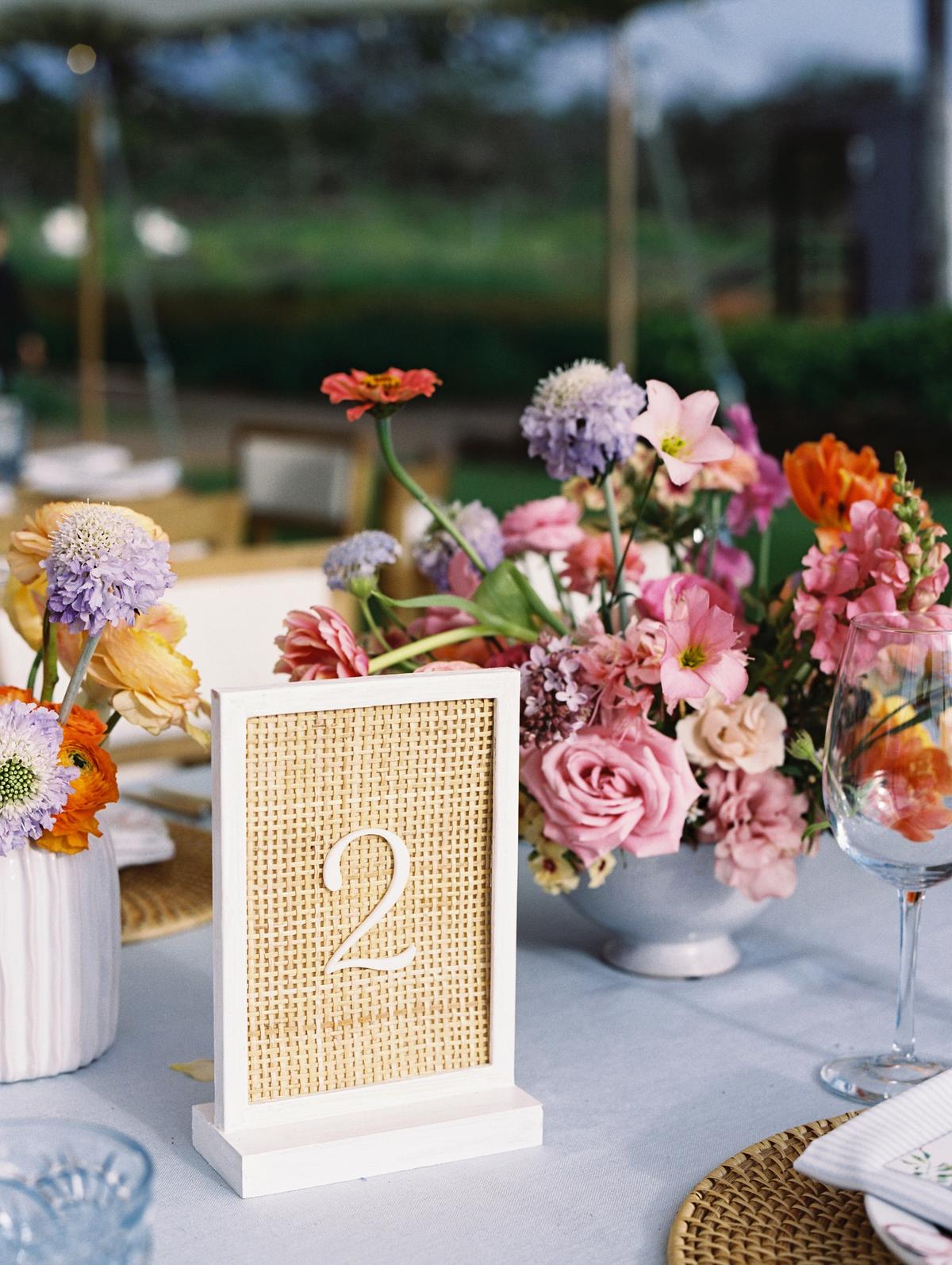 A reception table with pink and coral florals and a rattan table number card