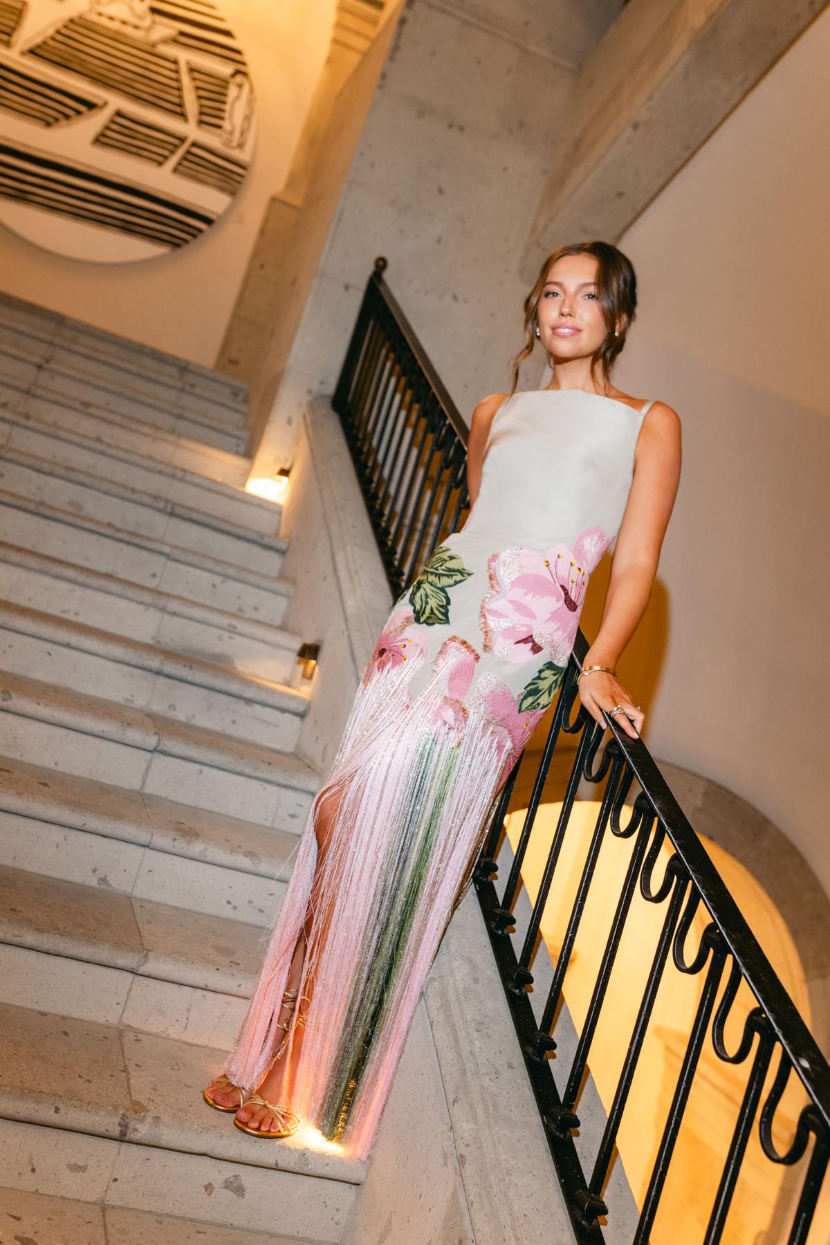 A bride in a floral fringed gown descends a staircase beside a wrought-iron railing
