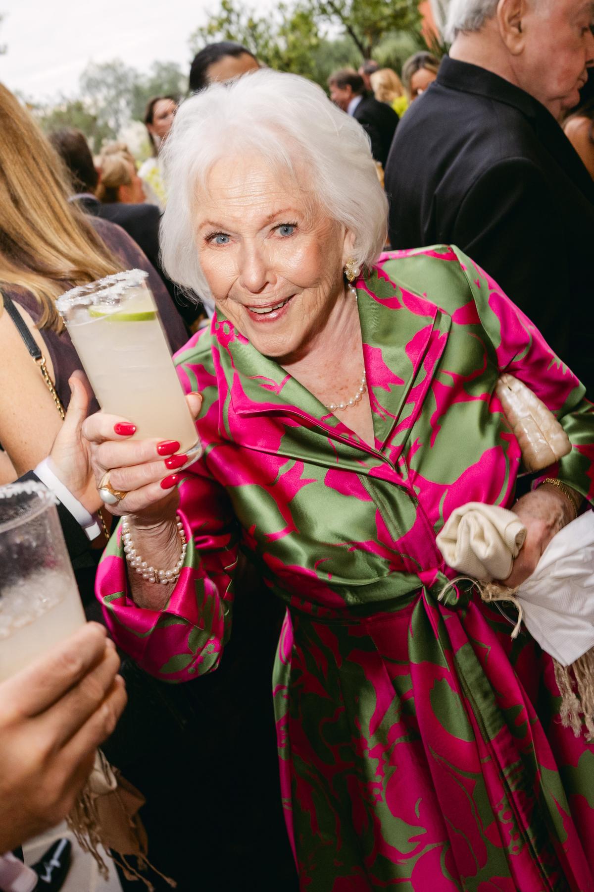 A wedding guest in a pink and green printed dress laughs while holding a margarita during cocktail hour