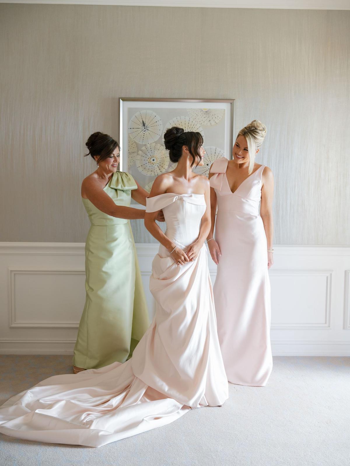 Bride in a strapless gown with two attendants adjusting the train in a bright room