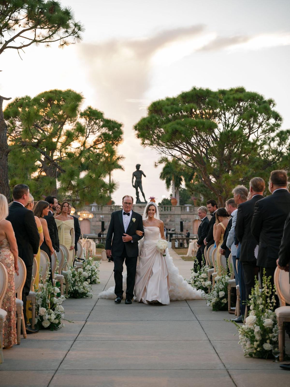 Couple walking back down the aisle between standing guests under oak trees