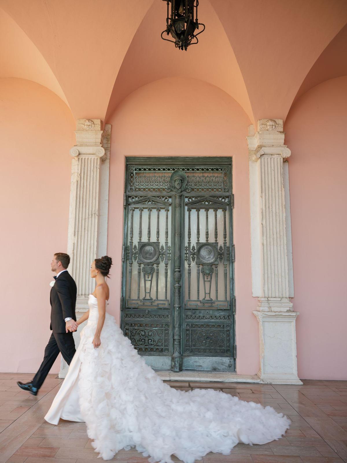 Bride and groom on stone steps in front of a pink archway and antique doors
