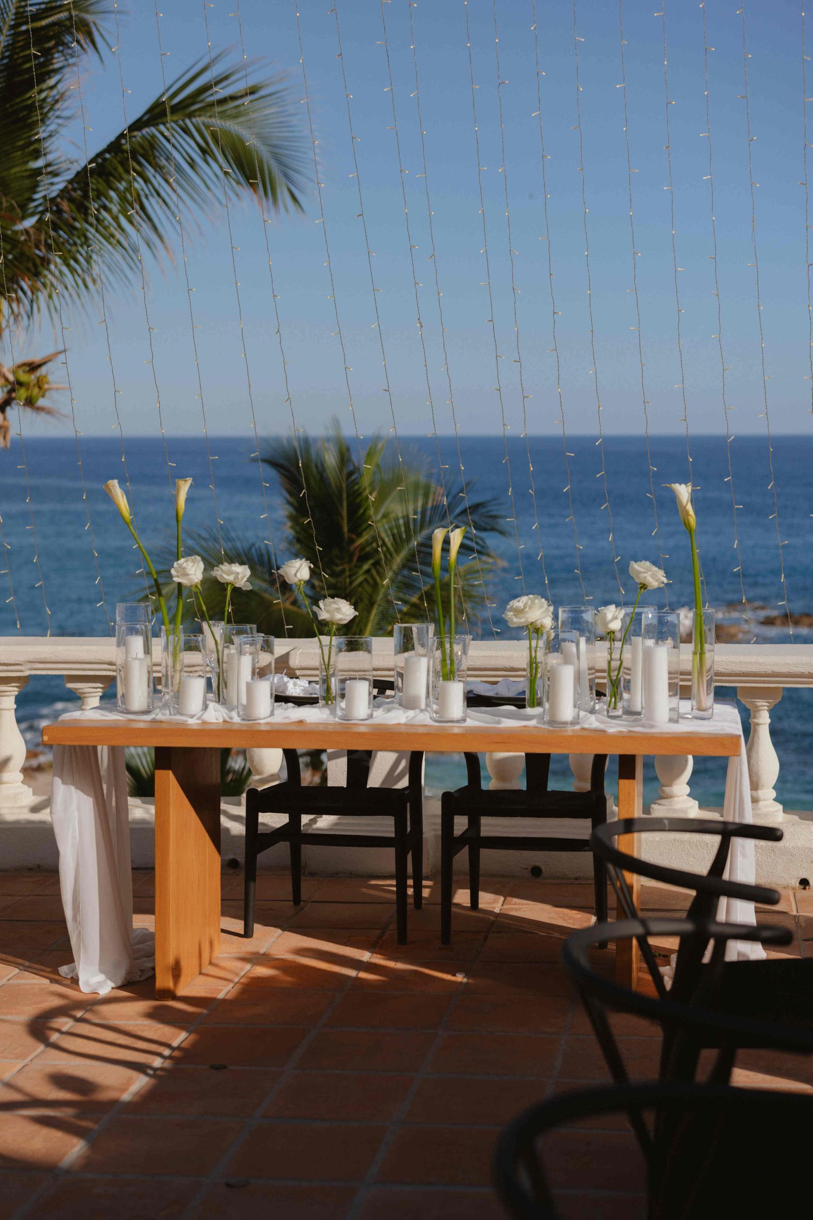 A long reception table set with candles and white flowers on a terrace overlooking the sea