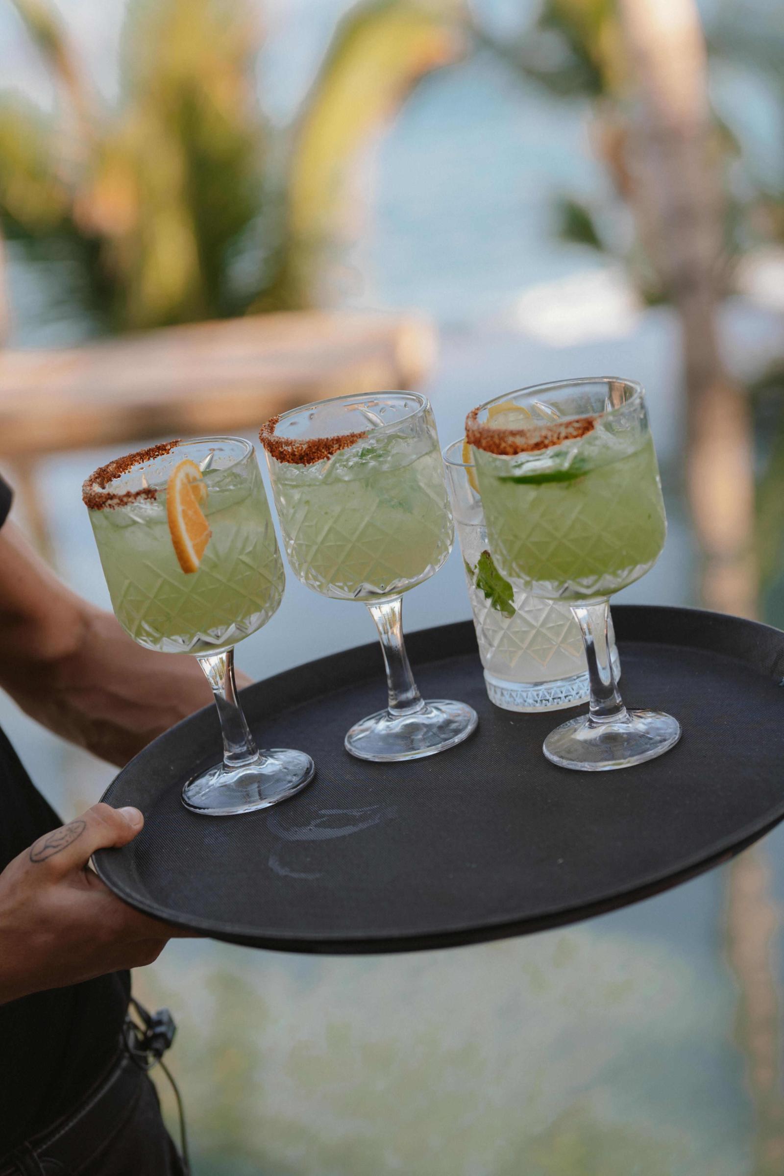 A server carries a tray of green cocktails with salted rims