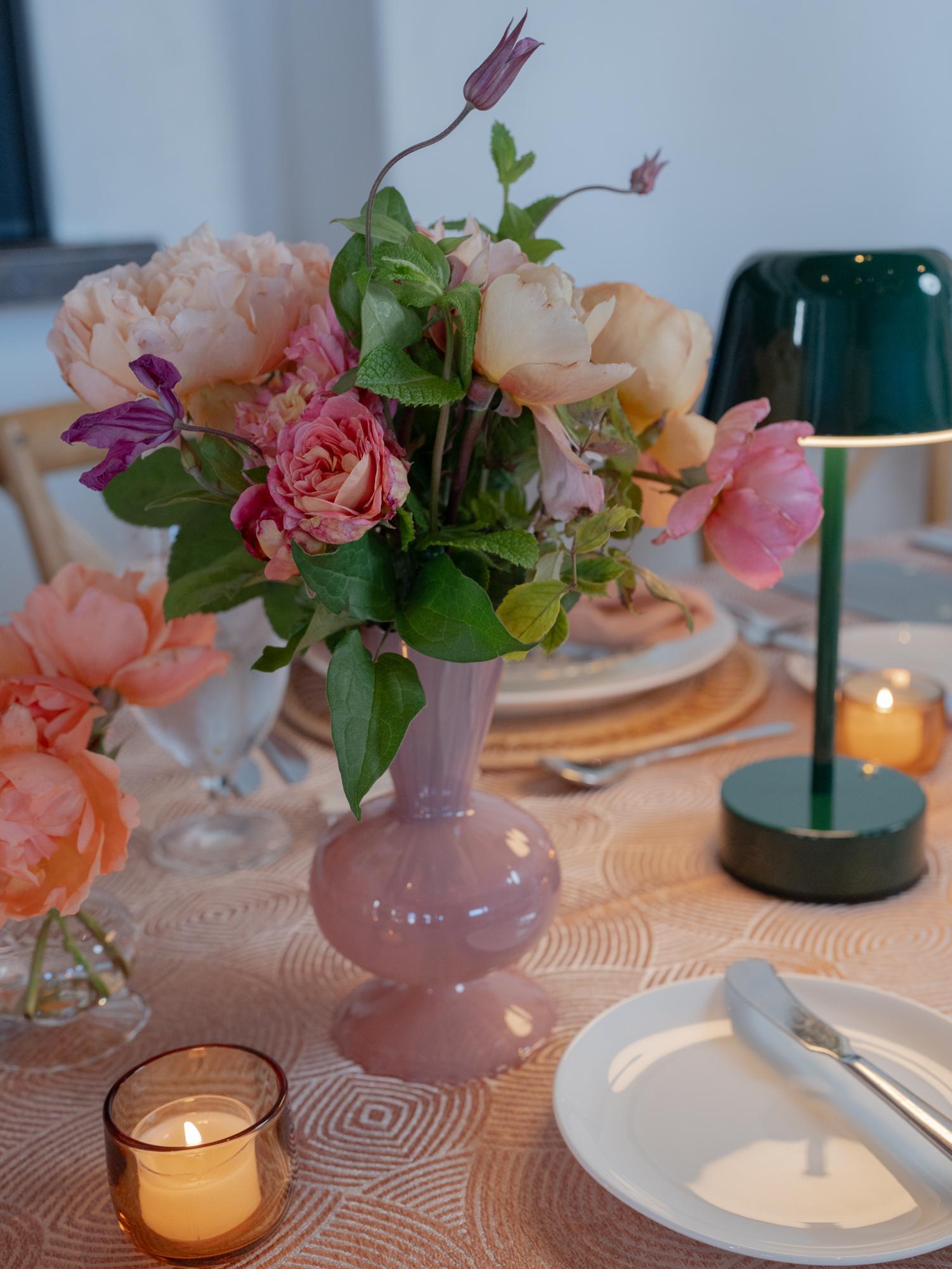 A reception table with a pink vase of garden roses, a green lamp and candlelight